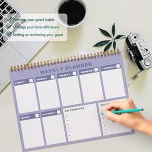 Lavender weekly planner pad on a desk with a laptop and coffee.