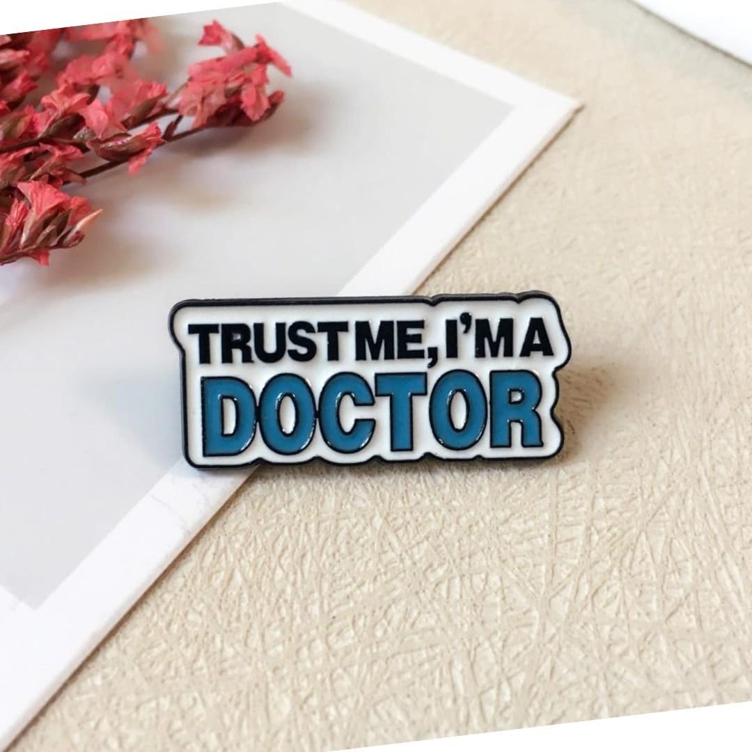 Trust me I'm a doctor enamel pin bold black blue typography funny medical lapel pin flat lay