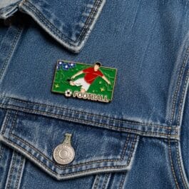 Football player enamel pin with green field and gold border on white background