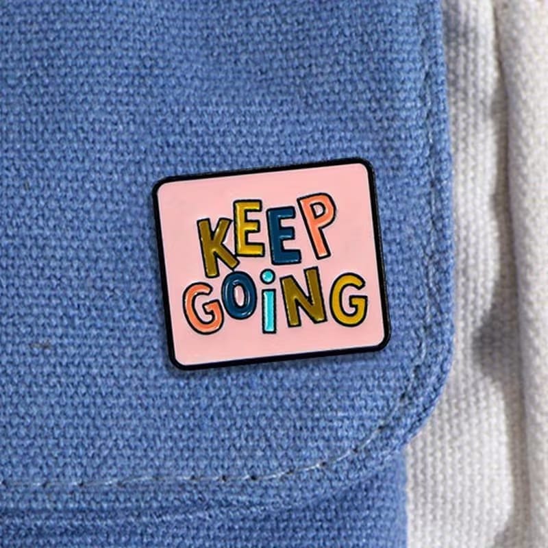 Keep Going enamel pin with colourful lettering on a pink background