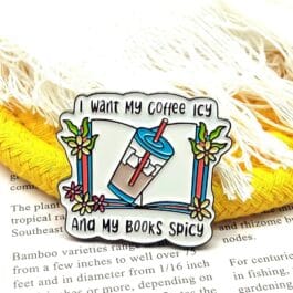Metal lapel pin with white book and blue iced coffee illustration featuring the quote "I want my coffee icy and my books spicy"
