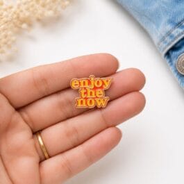 Enjoy The Now enamel pin with gold finish on white background