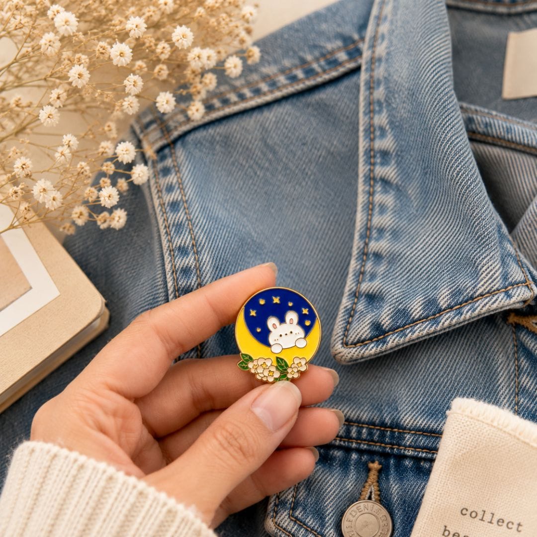 Blue and yellow bunny enamel pin with flowers and butterfly clasp held in hand