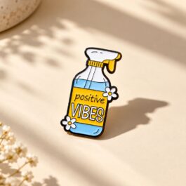 Positive Vibes soft enamel spray-bottle pin displayed on blue denim fabric.